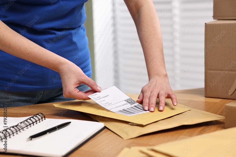 Poster Parcel packing. Post office worker sticking barcode on bag at wooden table indoors, closeup