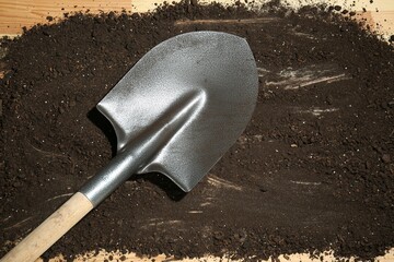 Metal shovel and soil on wooden surface, top view