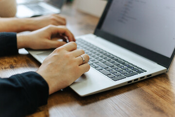 Hands typing on laptop's keyboard in office, programming