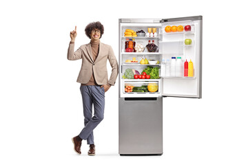 Happy young man pointing up and standing next to a fridge