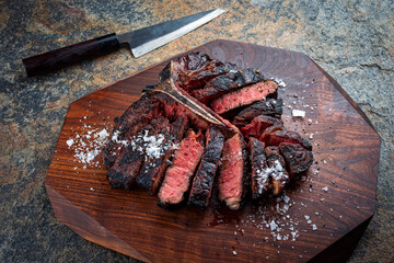 Traditional barbecue dry aged wagyu porterhouse beef steak bistecca alla Fiorentina sliced with salt and pepper served as close-up on a wooden design board with a Japanese knife