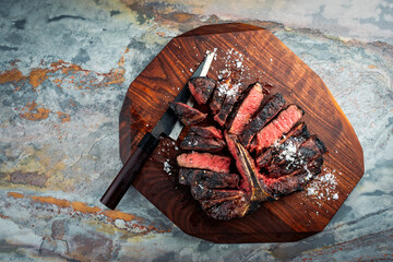 Traditional barbecue dry aged wagyu porterhouse beef steak bistecca alla Fiorentina sliced with salt and pepper served as top view on a wooden design board with a Japanese knife