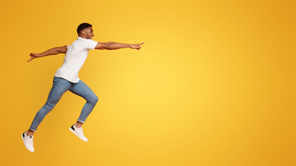 Fototapeta na wymiar Happy african guy jumping in air, reaching hand aside to free space