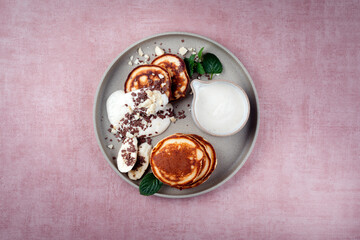 Traditional American Pancakes with banana honey cream, macadamia nuts and chocolate crumbles served as top view on a Nordic design plate