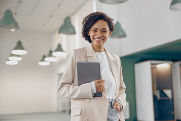 Smiling business woman with digital tablet standing on modern office background and looks camera