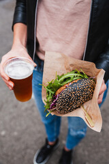 Close up of woman hands holding delicious organic salmon vegetarian burger and homebrewed IPA beer on open air beer an burger urban street food festival in Ljubljana, Slovenia