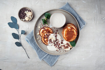 Traditional American Pancakes with banana honey cream, macadamia nuts and chocolate crumbles served as top view on a Nordic design plate