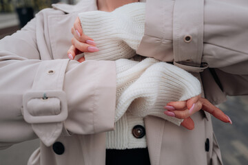 Street style cloth fashion details of a knitted white button-up sweater and beige women's trench...