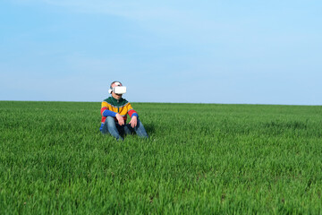 Man sitting on green grass in virtual reality glasses of the blue sky on the background, low...