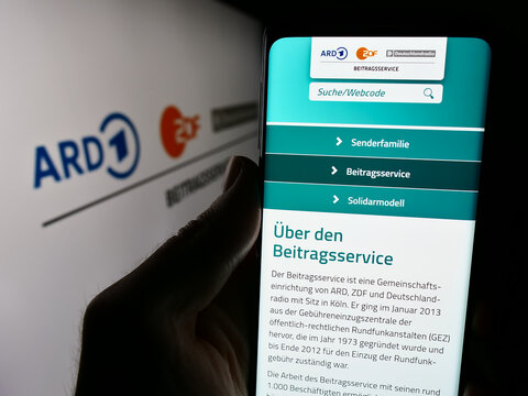 Stuttgart, Germany - 04-10-2024: Person holding cellphone with website of ARD ZDF Deutschlandradio Beitragsservice in front of logo. Focus on center of phone display.