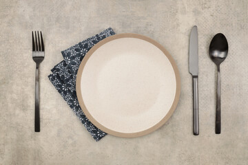 Empty plate, fork; knife, spoon, napkin on marble rustic concrete background. Top view, flat lay.