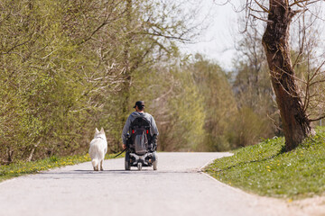 Man with disability outside in park with his service dog using electric wheelchair.