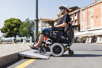 Male tourist on wheelchair crossing over the threshold ramp on the seaside promenade. Disability...