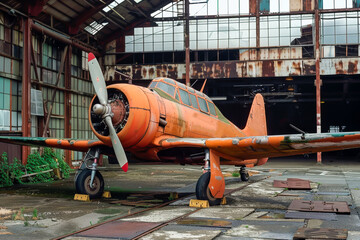 An old orange plane is sitting in a hangar. The plane is rusty and has a propeller