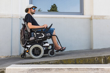 Man in an electric wheelchair using a building access ramp on a summer vacation. Accommodation,...