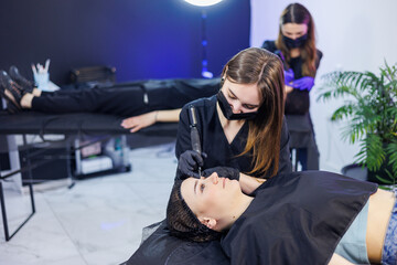 Obraz premium Permanent make-up of eyebrows. Woman professional permanent artist with a tool. A young permanent artist makes permanent eyebrow