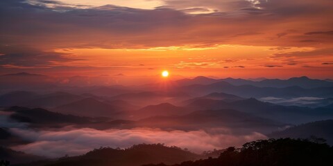 Obraz premium The sun is setting over a mountain range, casting a warm glow over the landscape. The sky is filled with clouds, creating a sense of mystery and tranquility. The mountains are covered in a mist