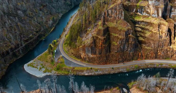 Wavy highway built around the bare rocks in Oregon State, USA. Beautiful narrow river flows at the foot of the mountains. Top view.