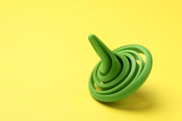 One green spinning top on yellow background, closeup. Space for text