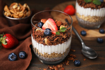 Tasty granola with berries, yogurt and chia seeds in glass on wooden table, closeup