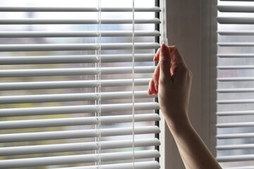 Woman opening white blinds at home, closeup