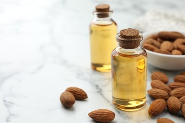 Almond oil in bottles and nuts on white marble table, closeup. Space for text