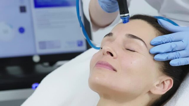 Beautician in gloves conducts vacuum cleaning and polishing face skin of young woman in cosmetology clinic. Professional moisturizing and rejuvenating hardware procedures for modern people.