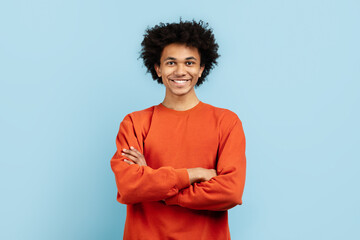 Confident guy crossing arms and smiling on blue background