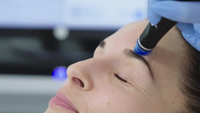 Beautician in gloves conducts vacuum cleaning and polishing face skin of young woman in cosmetology clinic. Professional moisturizing and rejuvenating hardware procedures for modern people.
