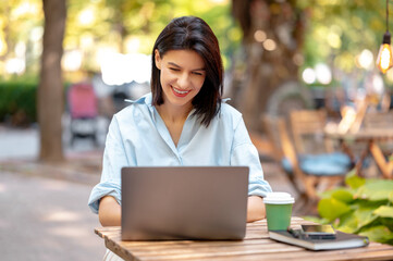 Young woman is using laptop for work and enjoying her morning coffee in park on a sunny day.