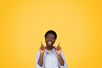 Smiling woman pointing upwards on yellow background
