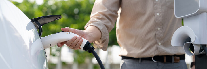 Young man recharge electric car's battery from charging station in city commercial parking lot....