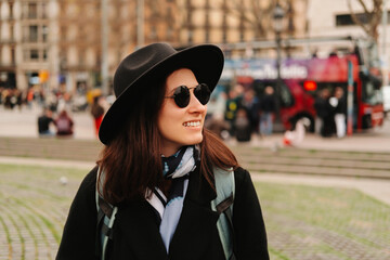 Outdoors shot of an ecstatic woman wearing hat, sunglasses, coat and backpack is enjoying the view while traveling in Spain.
