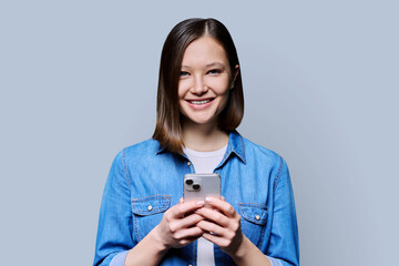 Young smiling woman using smartphone looking at camera in gray background