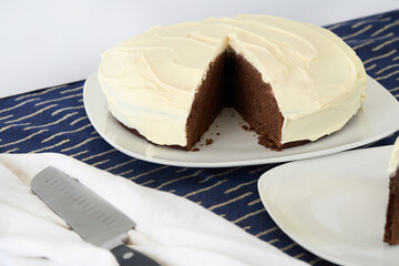 Round dark chocolate cake with delicate white frosting, with a slice taken out.
