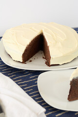Round dark chocolate cake with delicate white frosting, with a slice taken out.