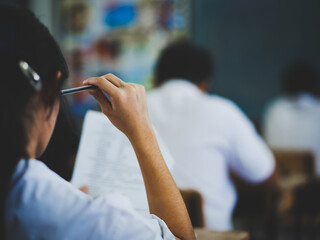 Students take exams with stress in the exam room.A female student thinks by holding a pencil next to her head