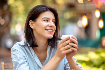 Close up shot of a smiling young woman enjoying her morning coffee in park in summer.