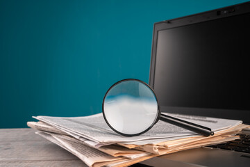Newspapers on laptop and magnifying glass, news, information concept, media