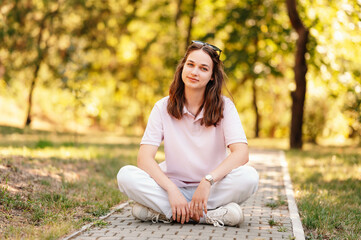 Portrait of a cheerful female student sitting and enjoying free time in park or campus.