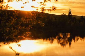 Outdoors landscape shot of a small lake with trees beside in spring at sunset. Warm colours.