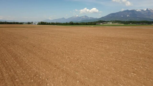 Fertile plowed arable land and a snowy mountains area in the background on a bright spring day, aerial shot. Agricultural fields and nature concepts.
