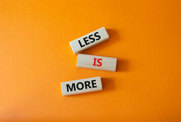 Less is More symbol. Concept words Less is More on wooden blocks. Beautiful orange background....