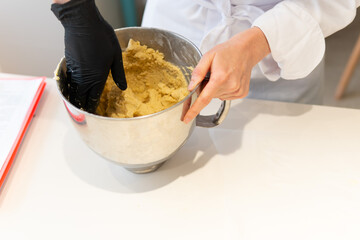Close-up of gloved hands kneading dough in a metal kitchen bowl. Handmade preparation by a professional pastry chef in uniform