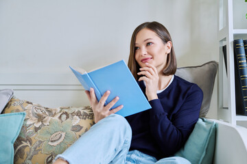 Young woman reading book, relaxed sitting on couch at home