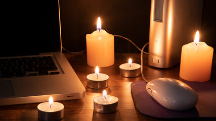 Blackout concept, 6 lit candles illuminating the workspace with a laptop
