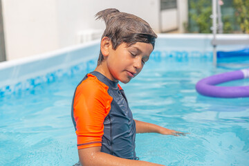 Young boy with eyes closed enjoying a moment in the pool, sun-kissed water sparkling around him