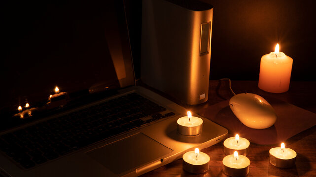 Blackout concept, 6 lit candles illuminating the workspace with a laptop