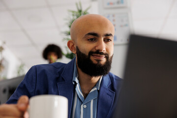 Smiling arab project manager checking customer email on laptop while working in business office....