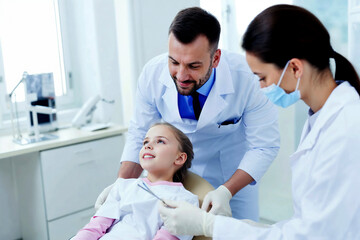Obraz premium A woman is seated in a chair while a dentist stands next to her, ready to perform a dental procedure.